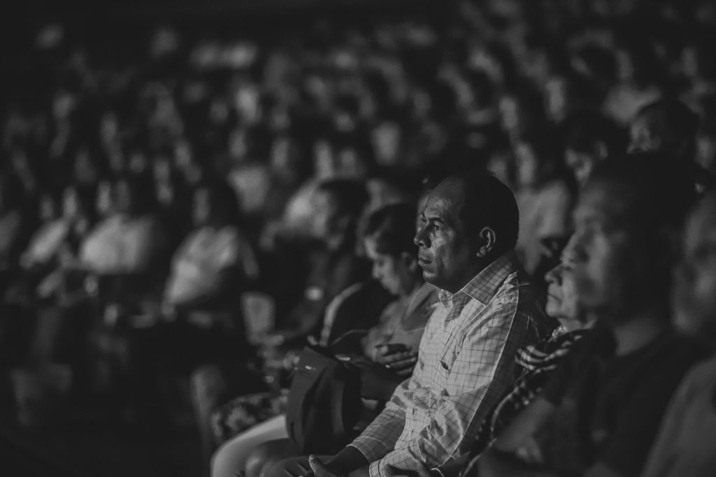 A serious audience at a monochrome event, focused and attentive in a crowded setting.